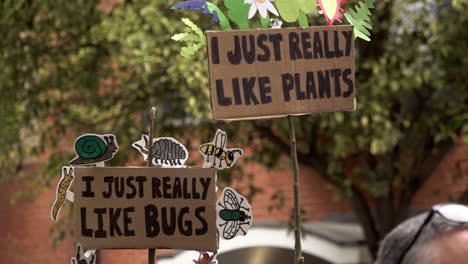 In-slow-motion-two-handmade-cardboard-protest-placards-read,-“I-just-really-like-plants”-and,-“-I-just-really-like-bugs”