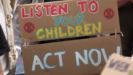 A-handmade-cardboard-protest-placard-is-held-that-reads,-“Listen-to-your-children,-act-now”-during-an-Extinction-Rebellion-demonstration