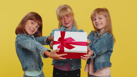 Three-girls-siblings-friends-presenting-birthday-gift-box-with-red-ribbon-holidays-sale-discount