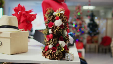 Close-up-shot-of-miniature-festive-Christmas-tree-crafted-from-pine-cones-sitting-on-clothing-store-display-table-next-to-stylish-neckties.-Xmas-decoration-in-empty-fashion-shop