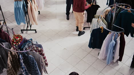 Top-down-view-of-customers-roaming-around-busy-shopping-mall-clothing-store-aisles,-looking-to-buy-clothes-as-gifts-for-family-and-friends-during-Christmas-promotional-sales-event