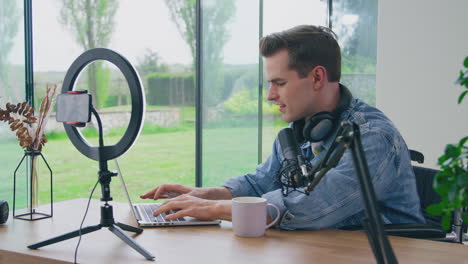 Male-Vlogger-Wearing-Headphones-With-Microphone-Typing-On-Laptop-Before-Live-Stream