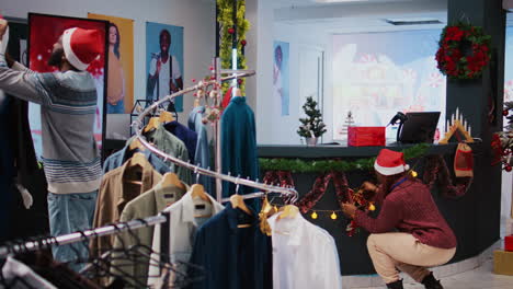 Afroamerikanische-Kollegen-Richten-Weihnachtsdekorationen-Im-Bekleidungsgeschäft-Eines-Einkaufszentrums-Ein.-Mitarbeiter-In-Festlicher-Stimmung,-Die-Modeboutique-Mit-Weihnachtsschmuck-Schmücken