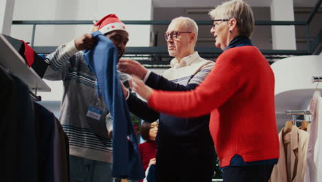 Elderly-couple-in-festive-adorn-shopping-mall-fashion-boutique,-being-helped-by-friendly-retail-assistant-with-finding-ideal-outfit-during-Chrismas-holiday-season-promotional-sales