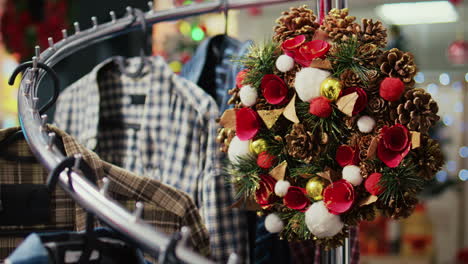 Dolly-out-shot-of-festive-Christmas-wreath-decorated-with-pine-cones-hanging-from-clothes-rack-in-empty-shopping-mall-store,-ready-to-bring-holiday-cheer-during-winter-holiday-season,-close-up