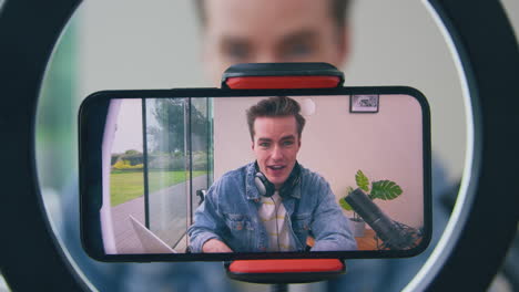 Male-Vlogger-Wearing-Headphones-With-Microphone-Live-Streaming-On-Mobile-Phone