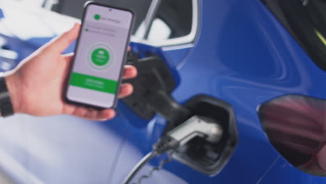 Man-Charging-Electric-Car-With-Cable-Using-App-On-Phone-To-Monitor-Charged-Battery-Level