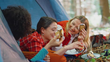 Group-Of-Female-Friends-On-Camping-Holiday-In-Forest-Lying-In-Tent-Eating-S'mores