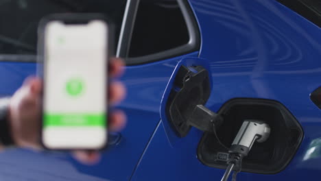 Man-Charging-Electric-Car-With-Cable-Using-App-On-Phone-To-Monitor-Battery-Level