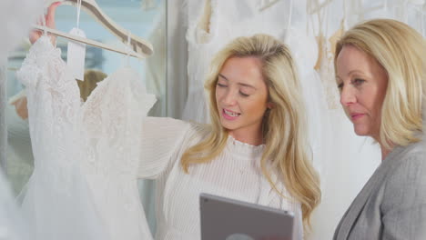 Verkäuferin-Mit-Digitalem-Tablet-Hilft-Frau-Bei-Der-Auswahl-Eines-Hochzeitskleides-Im-Brautmodengeschäft