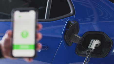 Mann-Lädt-Elektroauto-Mit-Kabel-über-App-Am-Telefon-Auf,-Um-Den-Batteriestand-Zu-überwachen