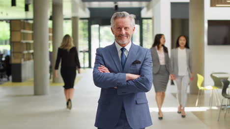 Portrait-Of-Senior-Businessman-CEO-Chairman-Standing-In-Lobby-Of-Busy-Modern-Office-Building