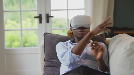 Woman-Relaxing-Lying-On-Sofa-At-Home-Wearing-VR-Headset-And-Interacting-With-AR-Technology