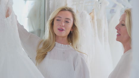 Mother-Helping-Adult-Daughter-To-Choose-Wedding-Dress-In-Bridal-Store