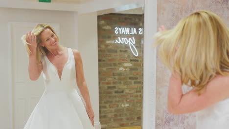 Lächelnde-Reife-Braut,-Die-Das-Hochzeitskleid-Im-Spiegel-Des-Brautmodengeschäfts-Betrachtet