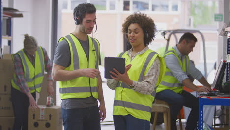 Male-And-Female-Workers-Wearing-Headsets-In-Logistics-Distribution-Warehouse-Using-Digital-Tablet