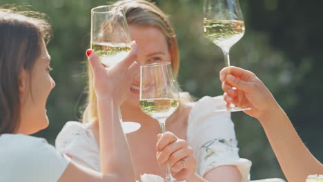 Three-Female-Friends-Sitting-Outdoors-In-Summer-Garden-At-Home-Drinking-Wine-And-Making-A-Toast