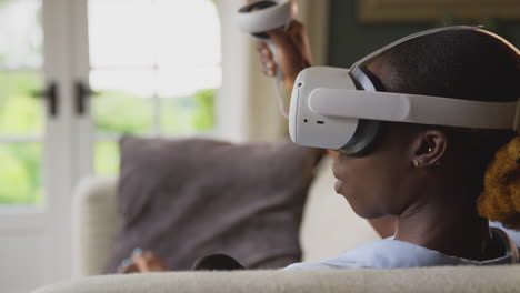 Frau-Liegt-Zu-Hause-Auf-Dem-Sofa,-Trägt-Ein-VR-Headset-Mit-Controllern-Und-Interagiert-Mit-AR-Technologie