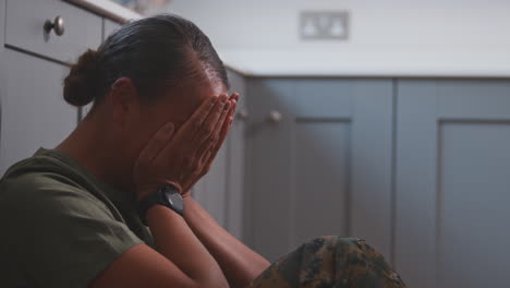 Depressive-Soldatin-In-Uniform,-Die-Unter-PTSD-Leidet-Und-Auf-Dem-Küchenboden-Auf-Heimaturlaub-Sitzt