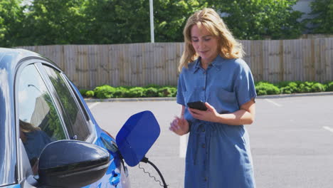 Woman-Charging-Electric-Car-With-Cable-Using-App-On-Phone-To-Monitor-Battery-Level