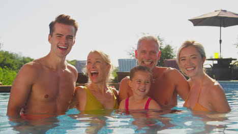 Portrait-Of-Smiling-Multi-Generation-Family-On-Summer-Holiday-Relaxing-In-Swimming-Pool