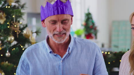 Multi-Generation-Family-Celebrating-Christmas-At-Home-Wearing-Paper-Hats-From-Crackers-Before-Meal