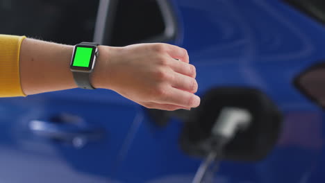 Frau,-Die-Elektroauto-Mit-Kabel-Auflädt,-Nutzt-App-Auf-Greenscreen-Smartwatch,-Um-Den-Batteriestand-Zu-überwachen