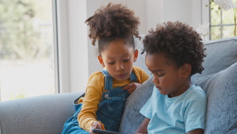 Boy-And-Girl-Playing-Handheld-Computer-Game-Sitting-On-Sofa-At-Home-Together