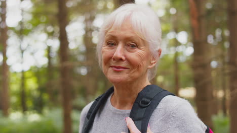 Vertical-Video-Of-Active-Retired-Senior-Woman-Walking-In-Woodland-Countryside-Wearing-Backpack