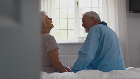 Worried-Retired-Senior-Couple-Sitting-On-Bed-At-Home-Talking-Together
