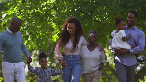Multi-Generation-Family-Holding-Hands-Enjoying-Summer-Walk-In-Countryside-Together