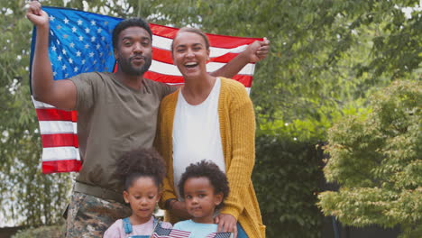 Portrait-Of-American-Army-Family-Outdoors-In-Garden-Holding-Stars-And-Stripes-Flag