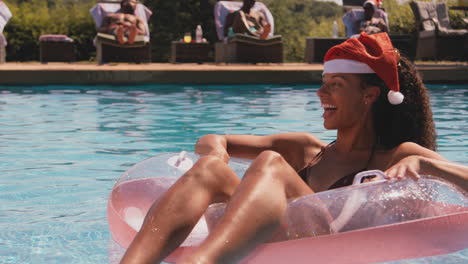 Woman-On-Christmas-Holiday-Floating-On-Inflatable-Ring-In-Swimming-Pool-Wearing-Santa-Hat