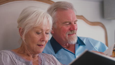Close-Up-Of-Retired-Senior-Couple-In-Bed-At-Home-Looking-At-Photo-Album-Together