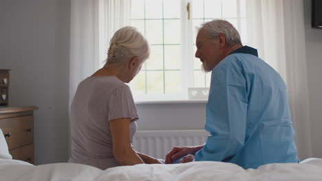 Worried-Retired-Senior-Couple-Sitting-On-Bed-At-Home-Talking-Together