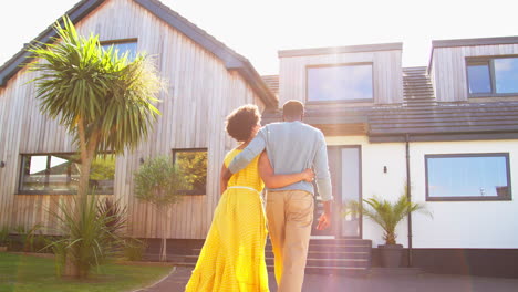 Rear-View-Of-Couple-Standing-In-Driveway-Walking-Towards-Dream-Home-Together