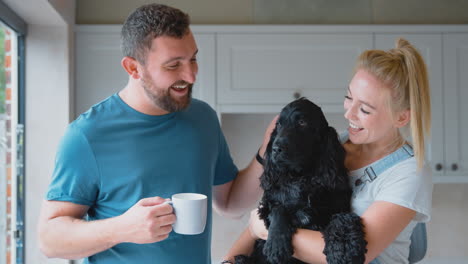Couple-On-Coffee-Break-From-Renovating-Kitchen-At-Home-Playing-With-Pet-Spaniel-Dog