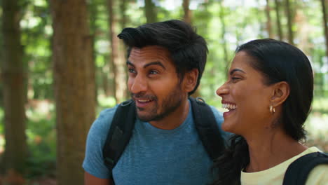 Couple-With-Backpacks-Hiking-Or-Walking-Through-Woodland-Countryside-In-Summer-Enjoying-Nature