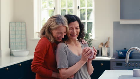 Loving-Same-Sex-Mature-Female-Couple-Drinking-Coffee-And-Hugging-In-Kitchen-Together