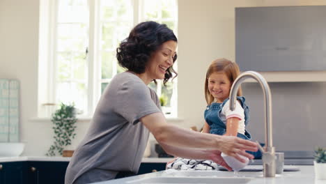 Family-With-Daughter-Helping-Older-Mother-To-Do-Washing-Up-In-Kitchen-At-Home