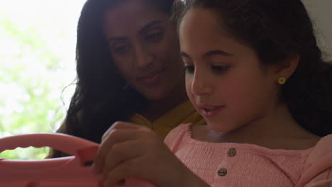 Close-Up-Of-Mother-And-Daughter-At-Home-Sitting-On-Sofa-Playing-Handheld-Computer-Game-Together