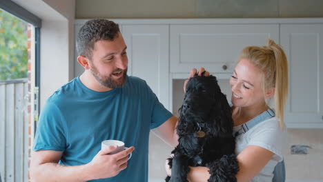 Couple-On-Coffee-Break-From-Renovating-Kitchen-At-Home-Playing-With-Pet-Spaniel-Dog