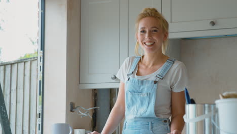 Portrait-Of-Smiling-Woman-Wearing-Dungarees-Renovating-Kitchen-At-Home