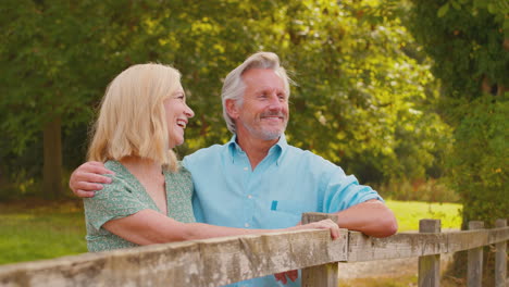 Smiling-Casually-Dressed-Mature-Or-Senior-Couple-Leaning-On-Fence-On-Walk-In-Countryside