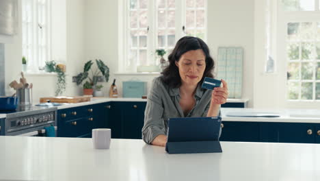 Reife-Frau-Mit-Kreditkarte-Nutzt-Digitales-Tablet-Zu-Hause,-Um-Urlaub-Zu-Buchen-Oder-Einzukaufen