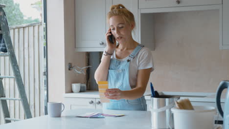 Mujer-Renovando-La-Cocina-En-Casa-Mirando-Muestras-De-Pintura-Y-Hablando-Por-Teléfono-Móvil.