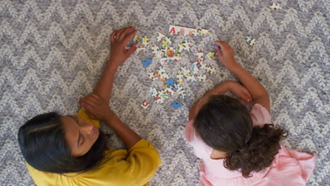 Overhead-Shot-Of-Mother-And-Daughter-At-Home-Lying-On-Floor-In-Lounge-Doing-Jigsaw-Puzzle-Together