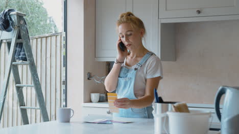 Frau-Renoviert-Zu-Hause-Die-Küche,-Schaut-Sich-Farbmuster-An-Und-Telefoniert