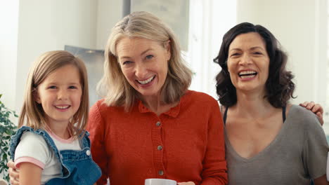 Portrait-Of-Multi-Generation-Female-Family-With-Same-Sex-Partner-Sitting-In-Kitchen-At-Home-Talking