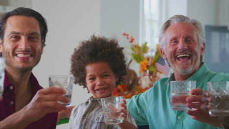 Familia-Multigeneracional-Celebrando-El-Día-De-Acción-De-Gracias-En-Casa-Comiendo-Y-Animando-Con-Agua